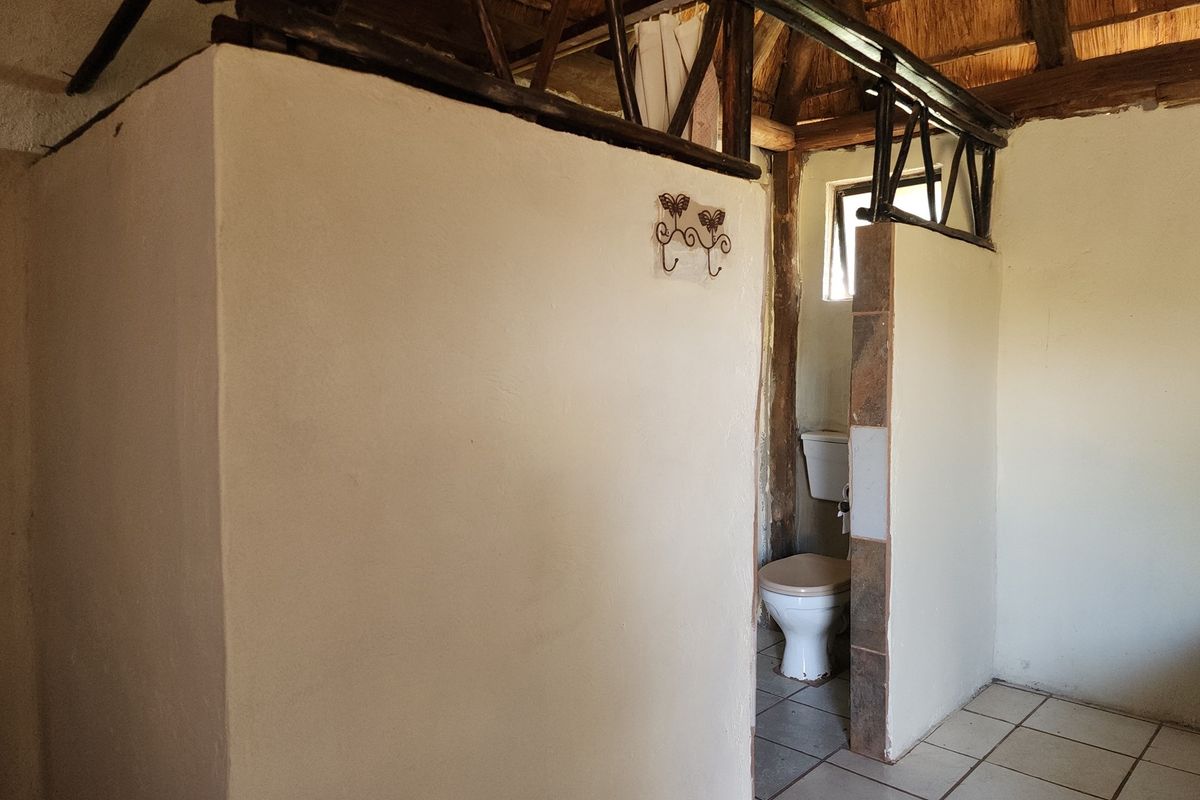 A rustic bathroom featuring a partitioned toilet area with exposed thatch roof beams and tiled flooring.
