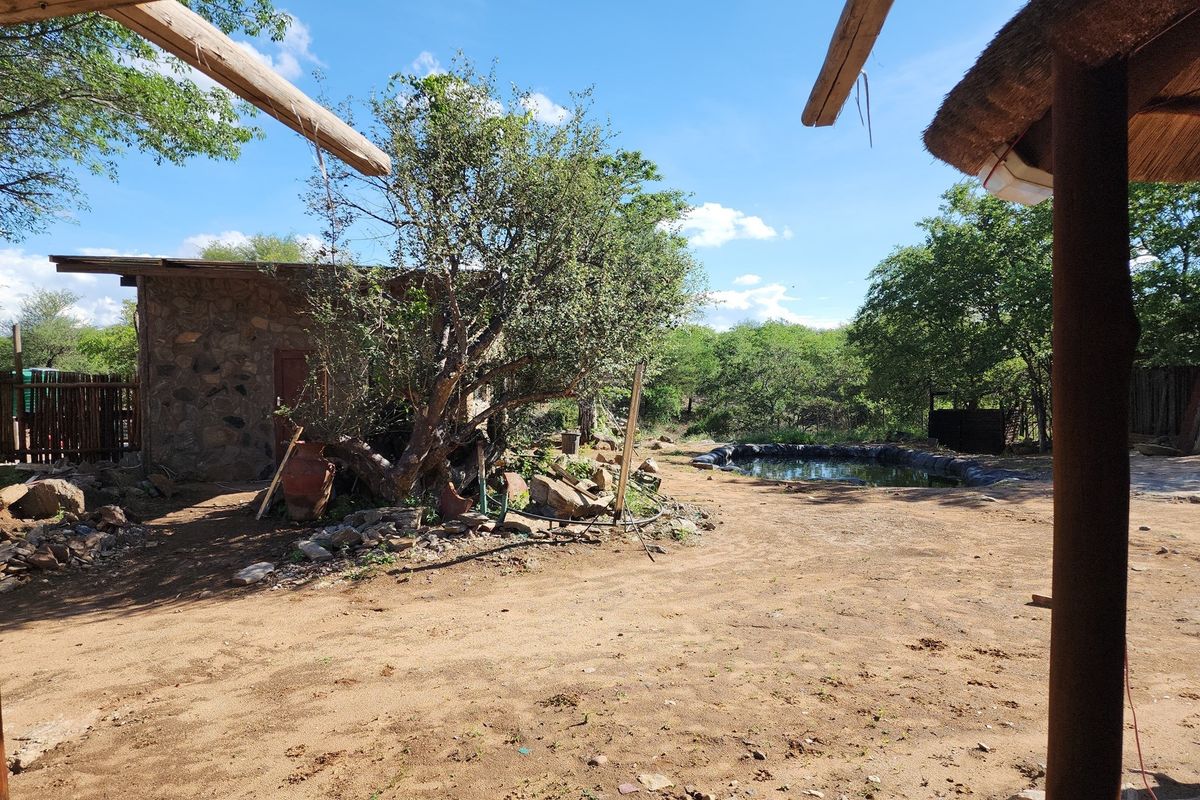 Outdoor farm area featuring a stone-clad structure, natural landscape, and a small water feature, offering a rustic and undeveloped rural setting.