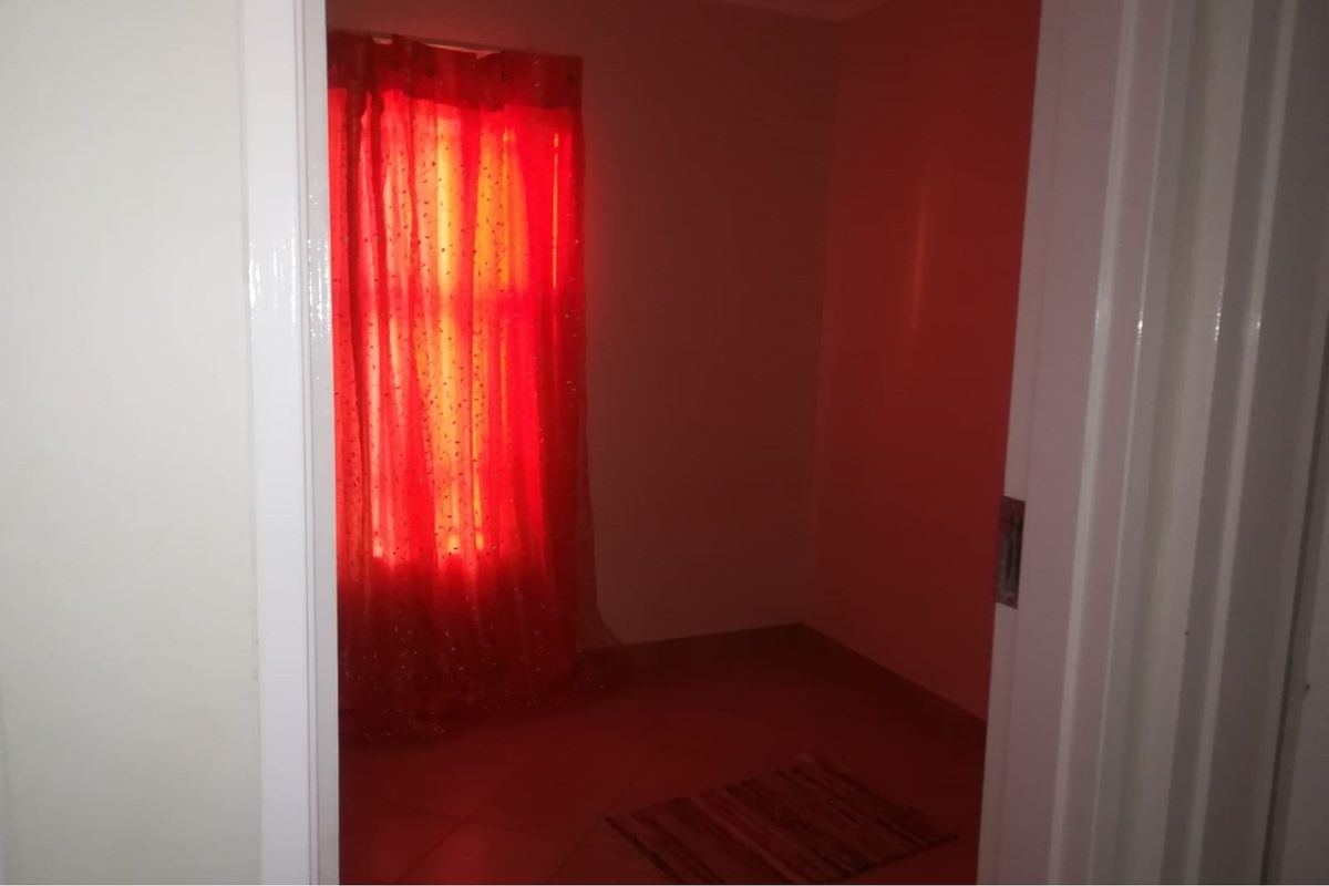 A view into a bedroom space featuring tiled flooring and a window with red curtains.