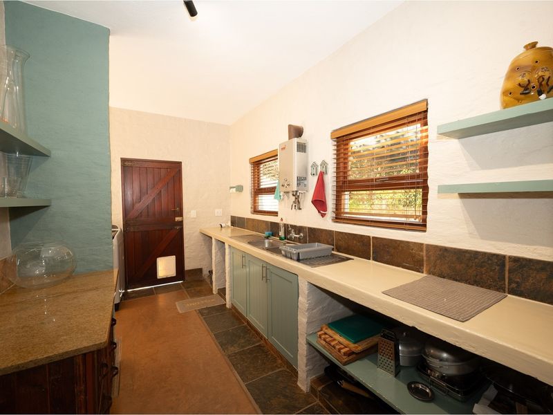 A functional scullery area featuring built-in cabinetry, a stainless steel sink, tiled backsplash, and a gas water heater.