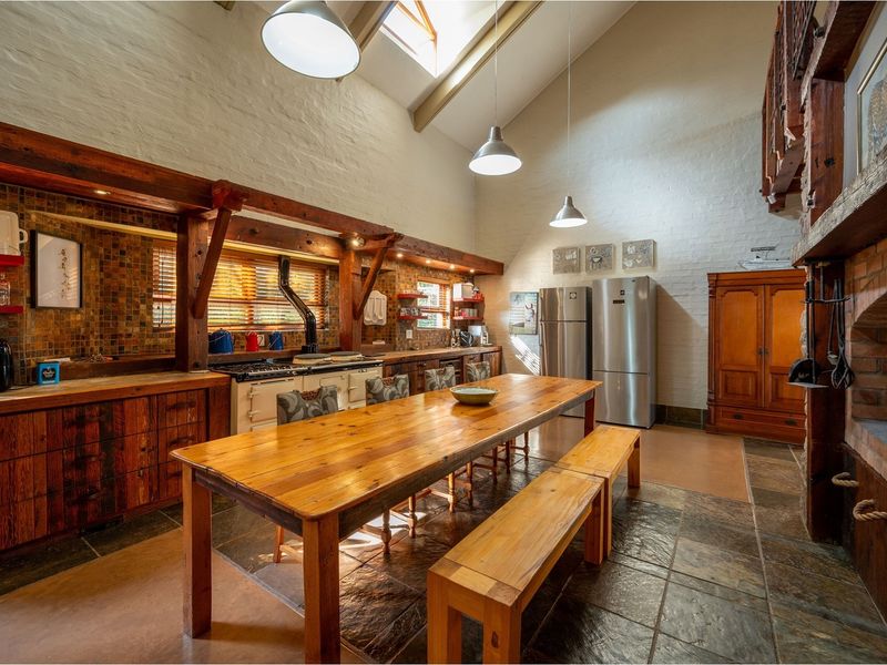 Spacious open-plan kitchen and dining area featuring vaulted ceilings, exposed timber beams, stone tile flooring, and a large built-in brick fireplace.