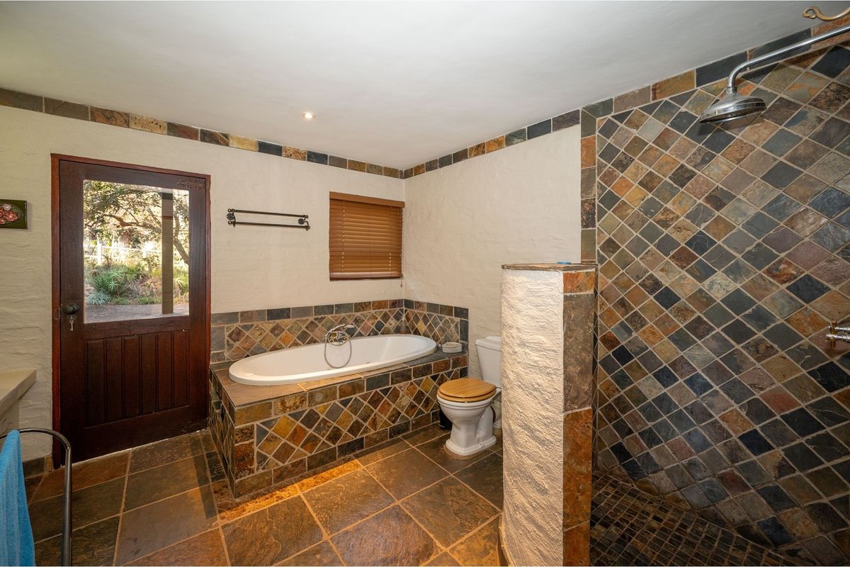 A rustic-style bathroom featuring a built-in bathtub, a walk-in shower with stone-look tiling, and direct access to the garden via a wooden door.