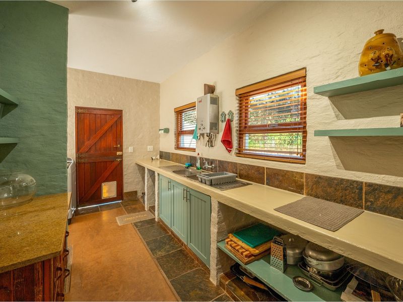 A functional scullery area featuring built-in concrete countertops, integrated cabinetry, a double sink, and a gas water heater.