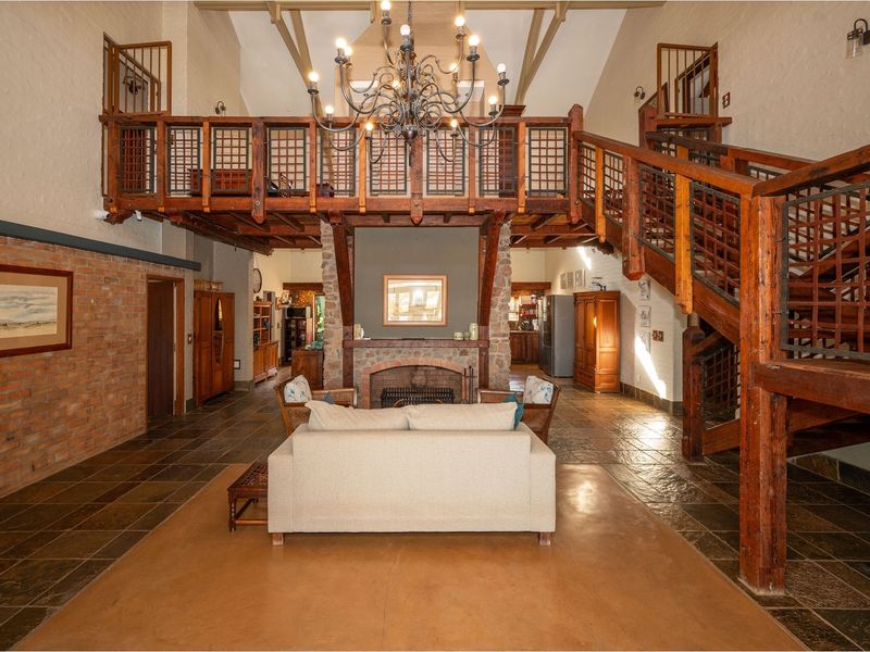 Spacious open-plan living area featuring a double-volume ceiling, exposed timber mezzanine, stone fireplace, and rustic slate flooring.