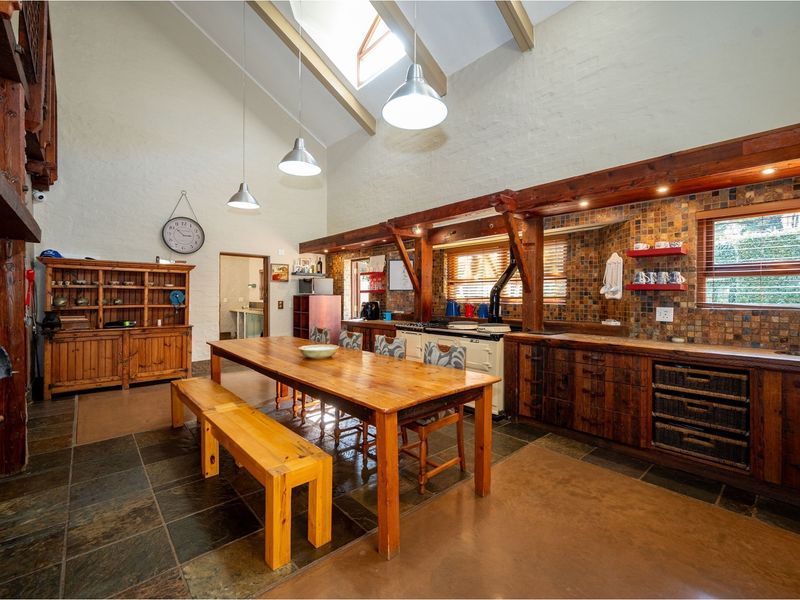 Spacious open-plan kitchen and dining area featuring high vaulted ceilings, exposed timber beams, slate flooring, and a large built-in wooden kitchen cabinetry unit.