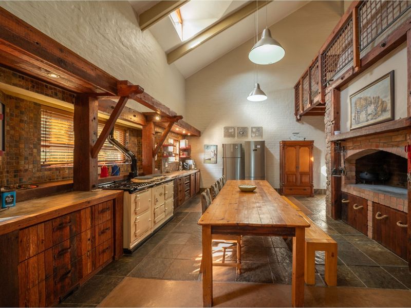 Spacious open-plan kitchen and dining area featuring rustic timber cabinetry, a large range cooker, stone flooring, and a prominent brick fireplace.