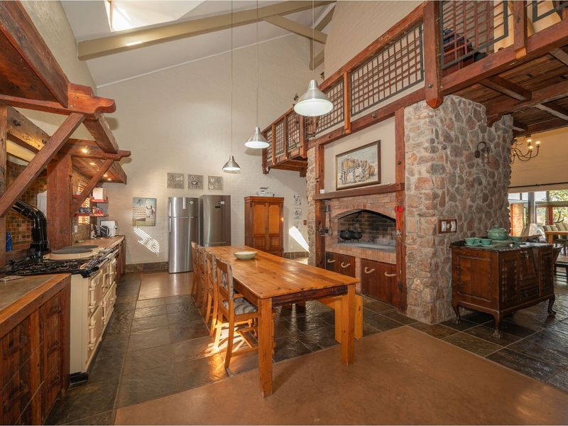 Spacious open-plan kitchen and dining area featuring a large stone fireplace, exposed timber beams, slate flooring, and a mezzanine level.