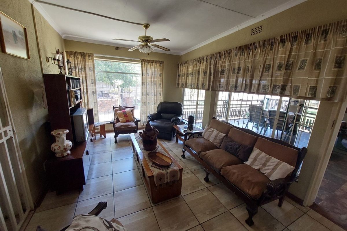 A living room featuring tiled flooring, a ceiling fan, and large windows providing natural light and access to the outdoor patio area.