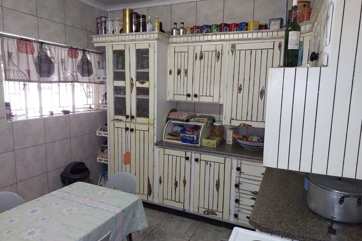 A dated kitchen featuring distressed-style cabinetry, tiled walls, and tiled flooring, offering a functional layout with ample storage space.