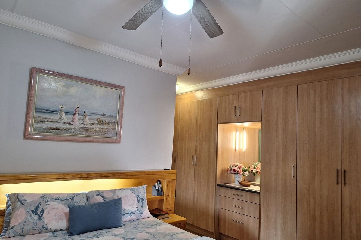 A well-maintained bedroom featuring extensive built-in wooden cabinetry, a vanity area with integrated lighting, and a ceiling fan.