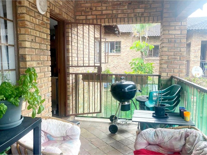 A covered balcony featuring exposed brick walls, tiled flooring, and a metal security gate, providing a functional outdoor space for relaxation.