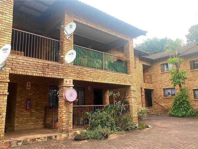 A multi-story apartment complex featuring a face brick facade, tiled roof, and paved courtyard with metal balcony railings.