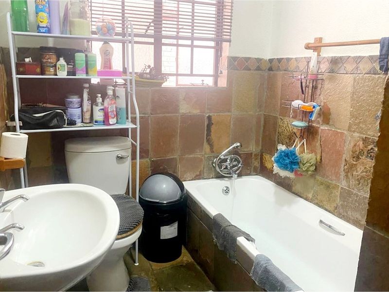 A functional bathroom featuring a bathtub, basin, and toilet with rustic stone-style wall tiling and a window for natural light.
