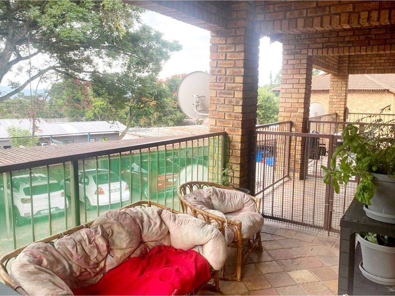 A covered balcony featuring brick pillars, metal railings, and tiled flooring, offering an outdoor space with views of the surrounding area.