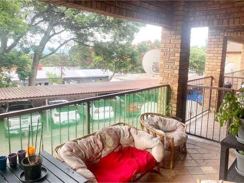 A covered balcony featuring brick pillars and tiled flooring, overlooking the complex parking area.