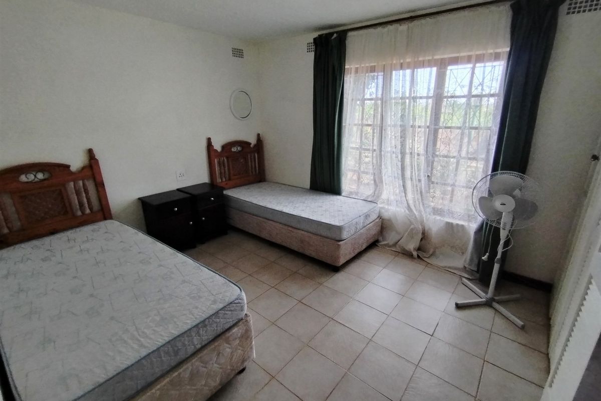 A bedroom featuring tiled flooring, large window with security bars, and neutral wall finishes.