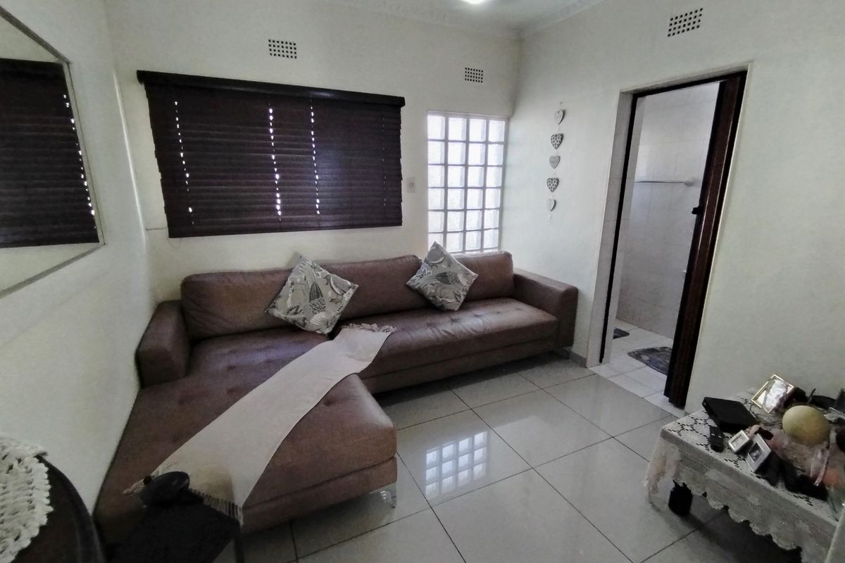 A living room featuring tiled flooring, a glass block window, and a dark roller blind, with an adjacent doorway leading to a bathroom.