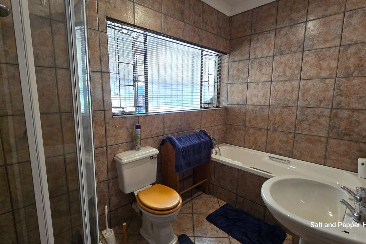 A functional bathroom featuring a built-in bathtub, separate shower enclosure, pedestal basin, and toilet, finished with full-height ceramic wall tiling.
