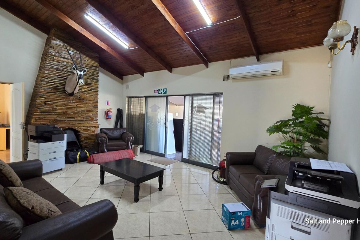 Spacious living area featuring a stone-clad fireplace, exposed timber beam ceiling, tiled flooring, and split-system air conditioning unit.