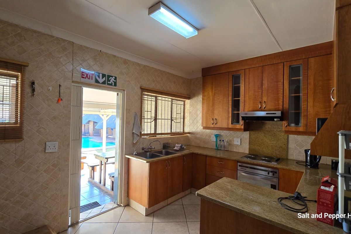 A functional kitchen featuring wooden cabinetry, stone countertops, a built-in oven and hob, and direct access to the outdoor pool area.