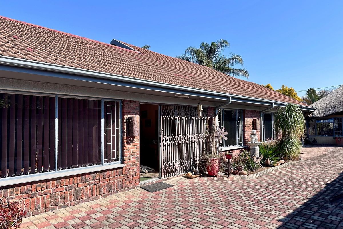 Rear view of the property featuring a brick facade, tiled roof, and a paved patio area with security gate access.