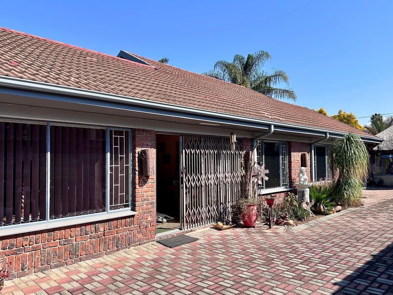 Rear view of the property featuring a brick facade, tiled roof, and a paved patio area with security gate access.