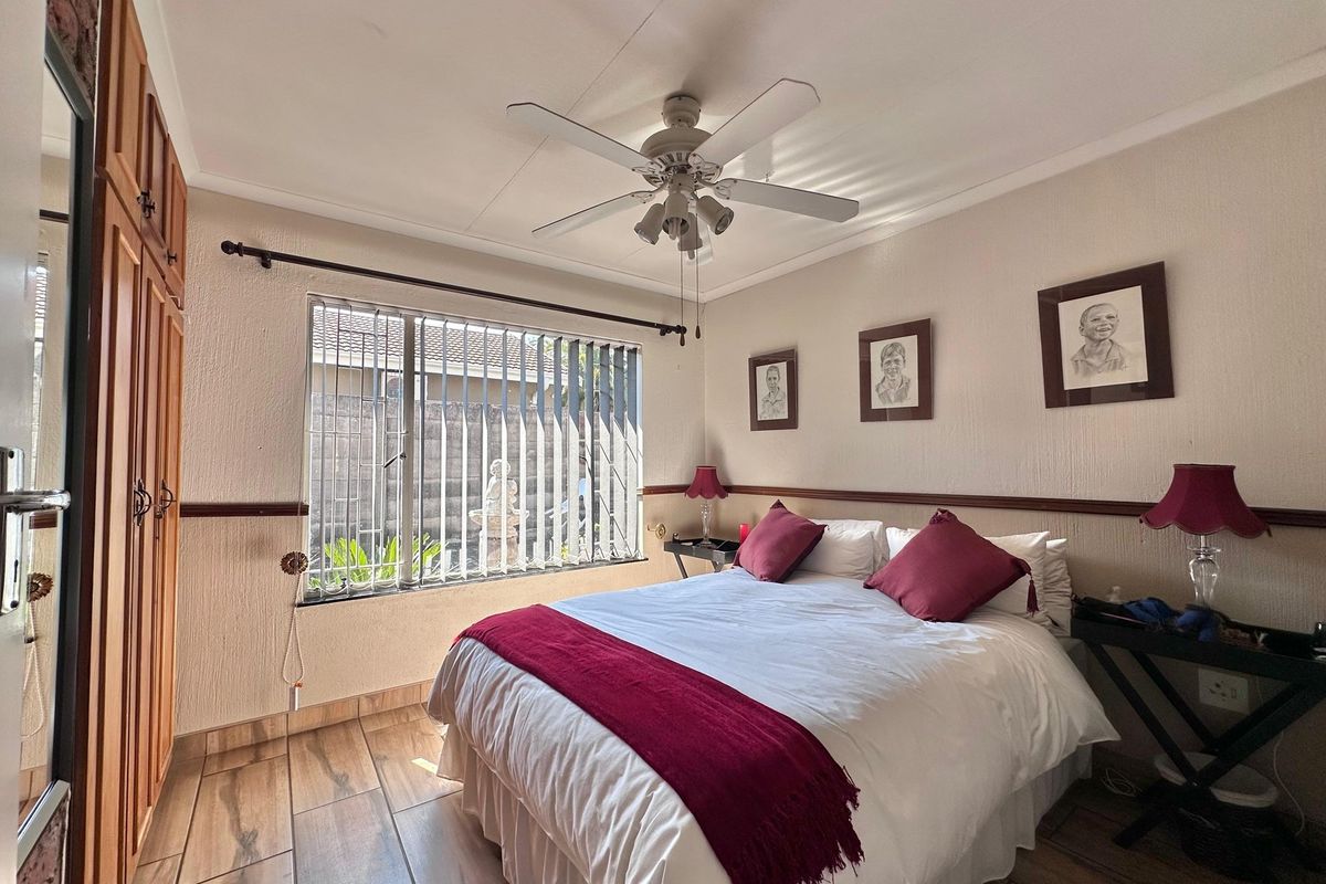 A bedroom featuring built-in wooden cupboards, tiled flooring, and a ceiling fan, with security bars installed on the window.