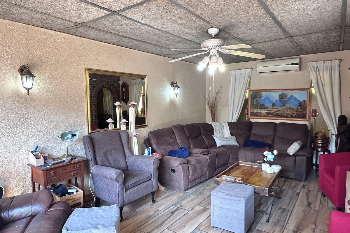 A comfortable living room featuring wood-look tile flooring, a ceiling fan, and a wall-mounted air conditioning unit.