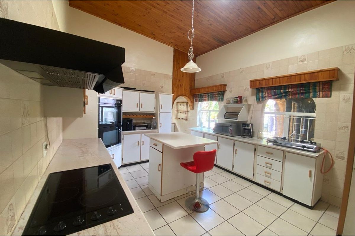 Spacious kitchen featuring white cabinetry, built-in oven, electric hob, extractor fan, and a central island, finished with tiled flooring and a timber-clad vaulted ceiling.
