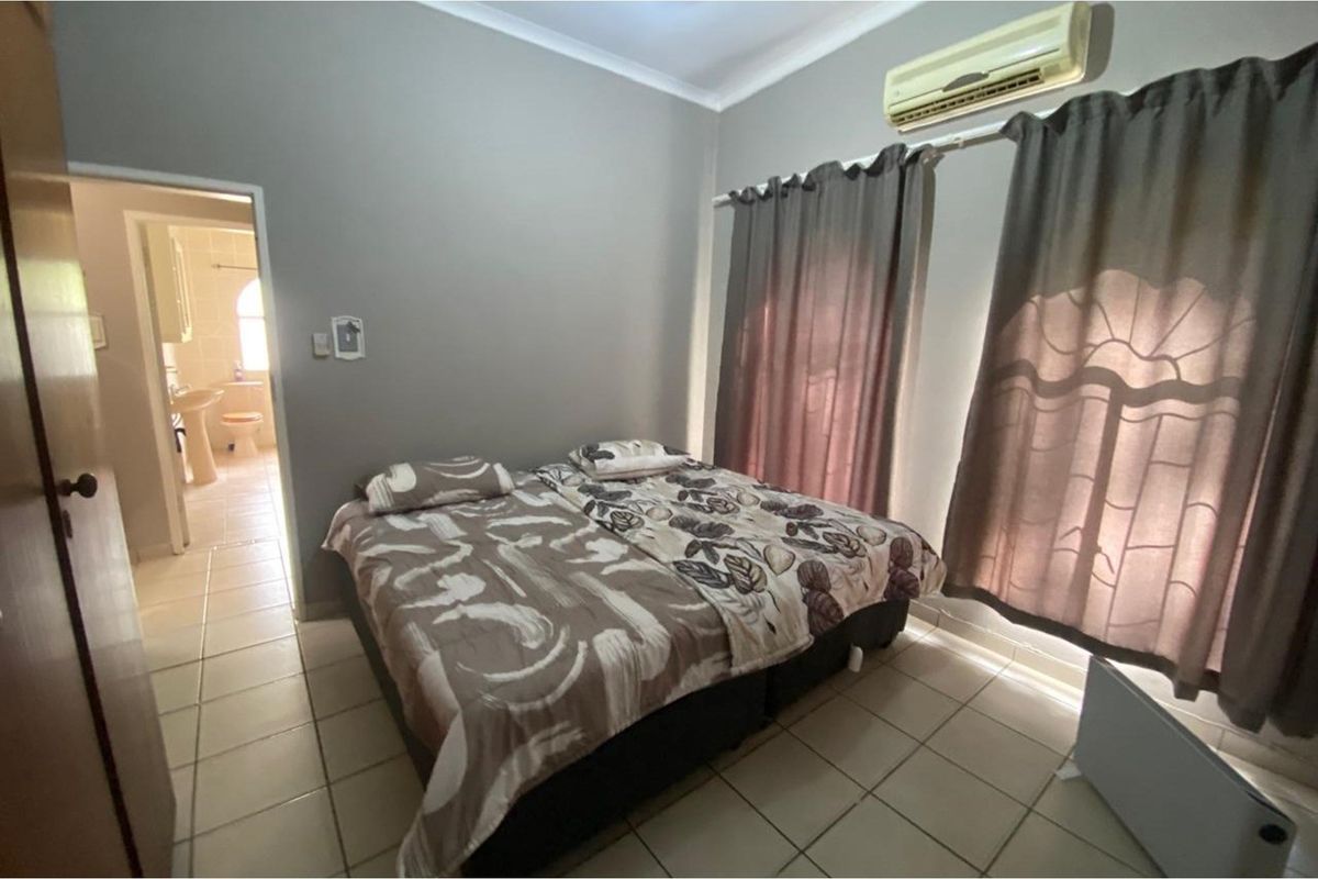 A bedroom featuring tiled flooring, a wall-mounted air conditioning unit, and an adjoining en-suite bathroom.