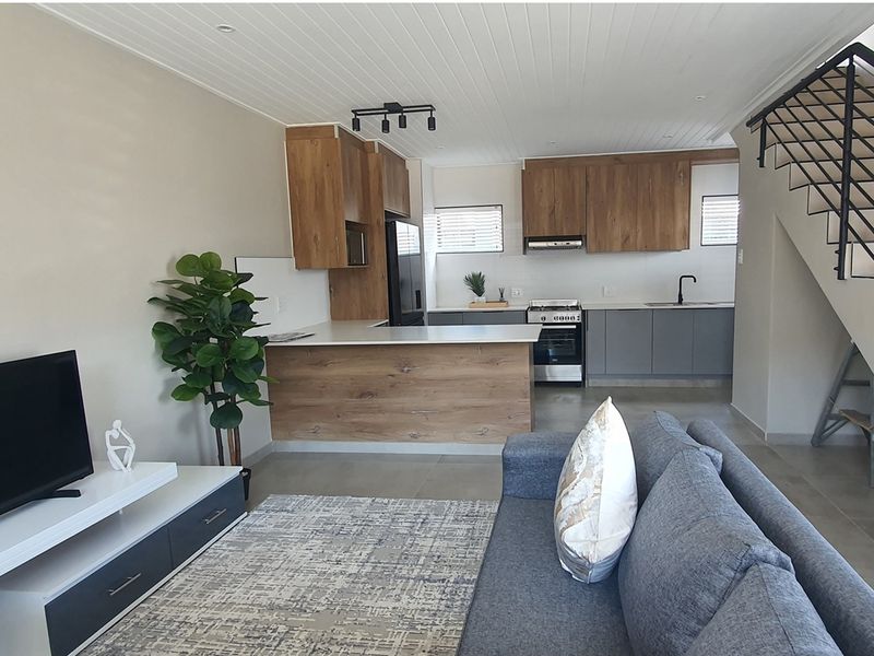Open-plan living area featuring a modern kitchen with wood-tone cabinetry, stone countertops, a gas stove, and a staircase with a metal balustrade.