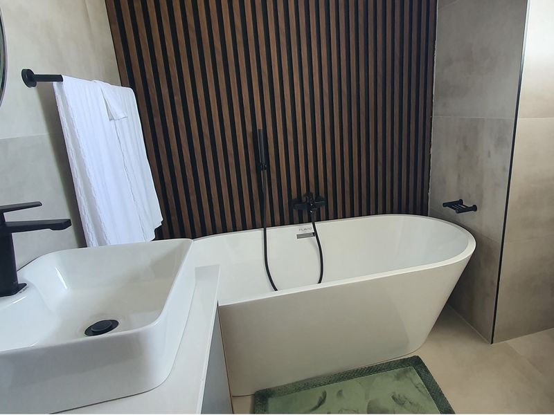 Modern bathroom featuring a freestanding bathtub, contemporary vessel sink, matte black fixtures, and a stylish timber slat feature wall.