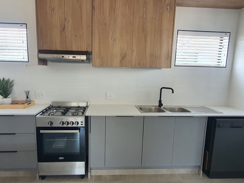 Modern kitchen featuring wood-look upper cabinetry, grey lower cabinets, a stainless steel gas stove with extractor fan, and a double sink with matte black faucet.