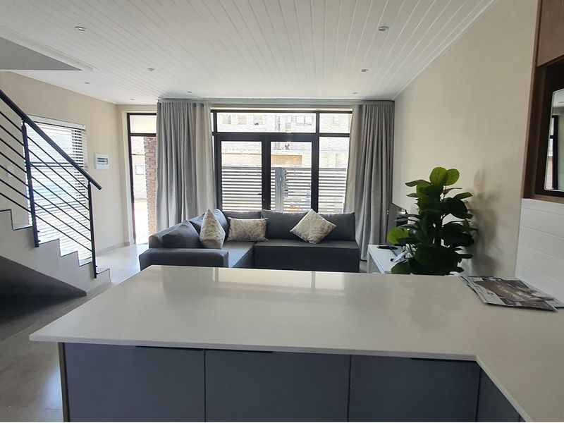 Open-plan living area featuring a modern kitchen island, staircase with metal balustrade, and large glass doors leading to an outdoor space.