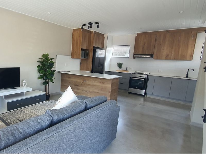 Modern open-plan living area featuring a contemporary kitchen with wood-tone cabinetry, stone countertops, integrated appliances, and sleek tiled flooring throughout.
