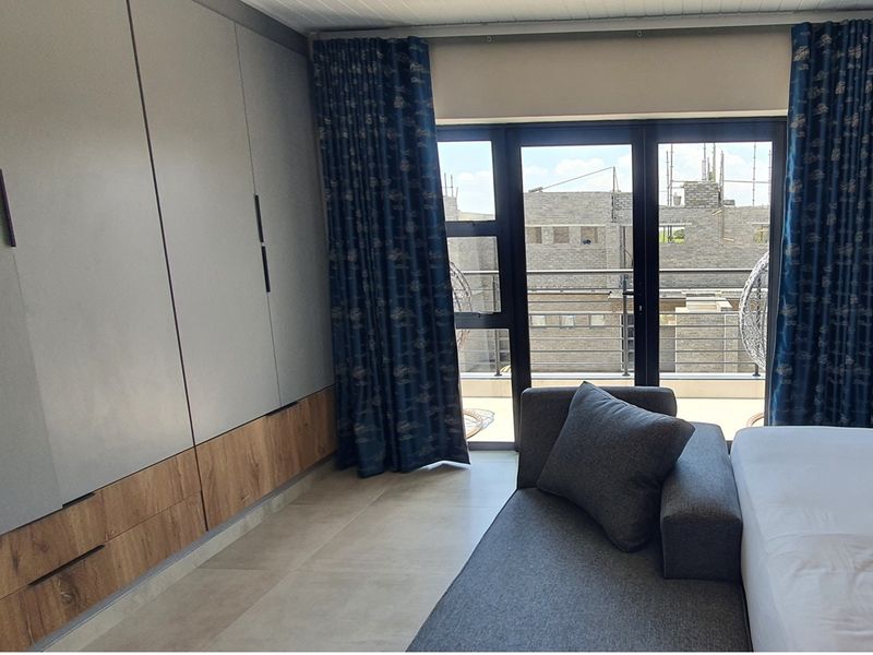 Modern bedroom featuring built-in floor-to-ceiling cabinetry with wood-grain accents, large glass sliding doors, and access to a private balcony.