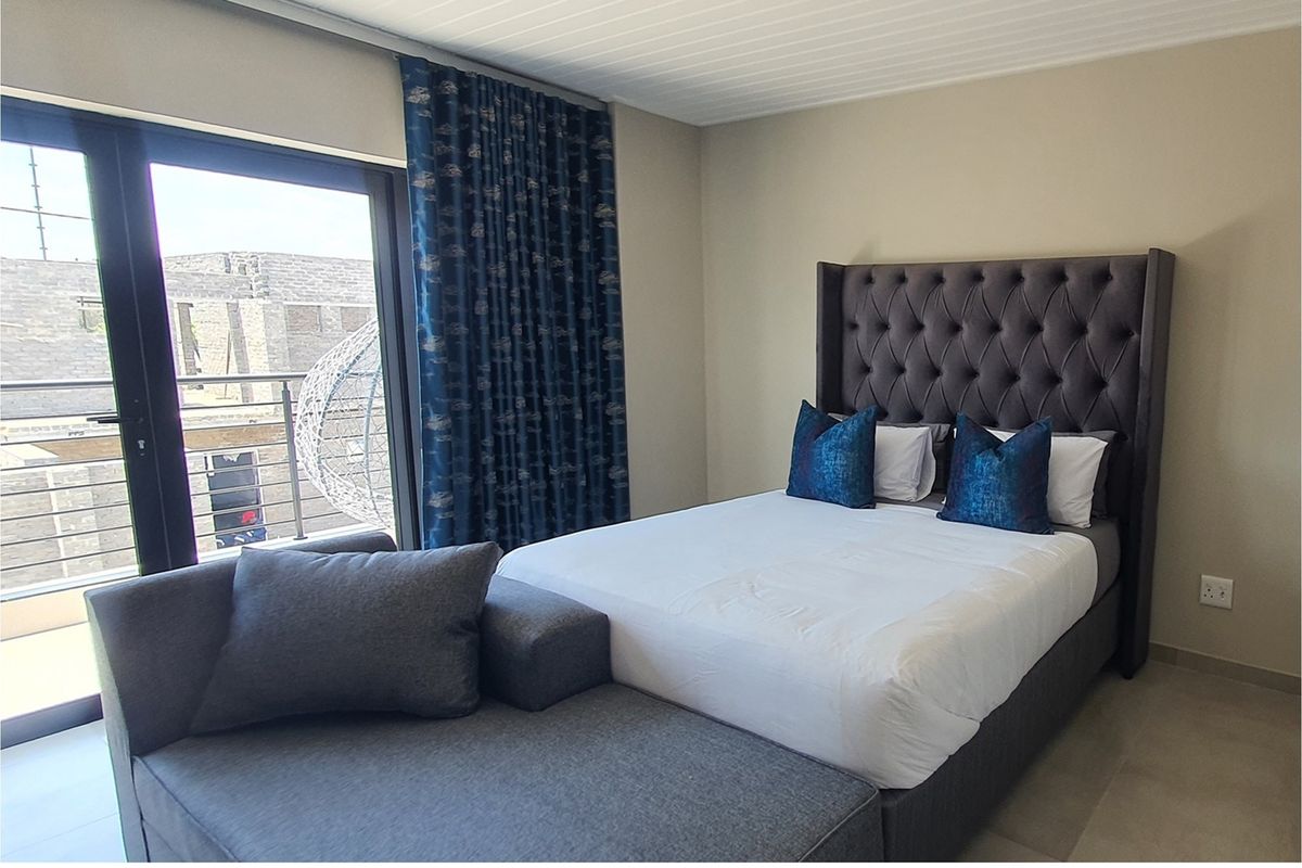 A well-maintained bedroom featuring neutral wall finishes, tiled flooring, and direct access to a private balcony through large glass sliding doors.
