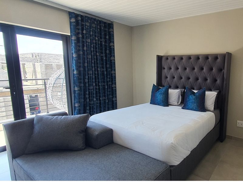 A well-maintained bedroom featuring neutral wall finishes, tiled flooring, and direct access to a private balcony through large glass sliding doors.