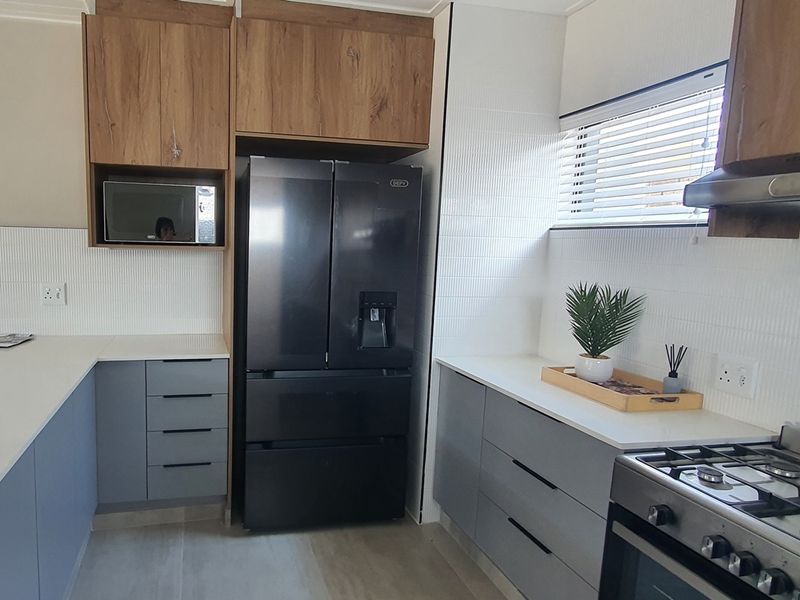 Modern kitchen featuring two-tone cabinetry, white tiled backsplash, stone countertops, and a built-in microwave space.