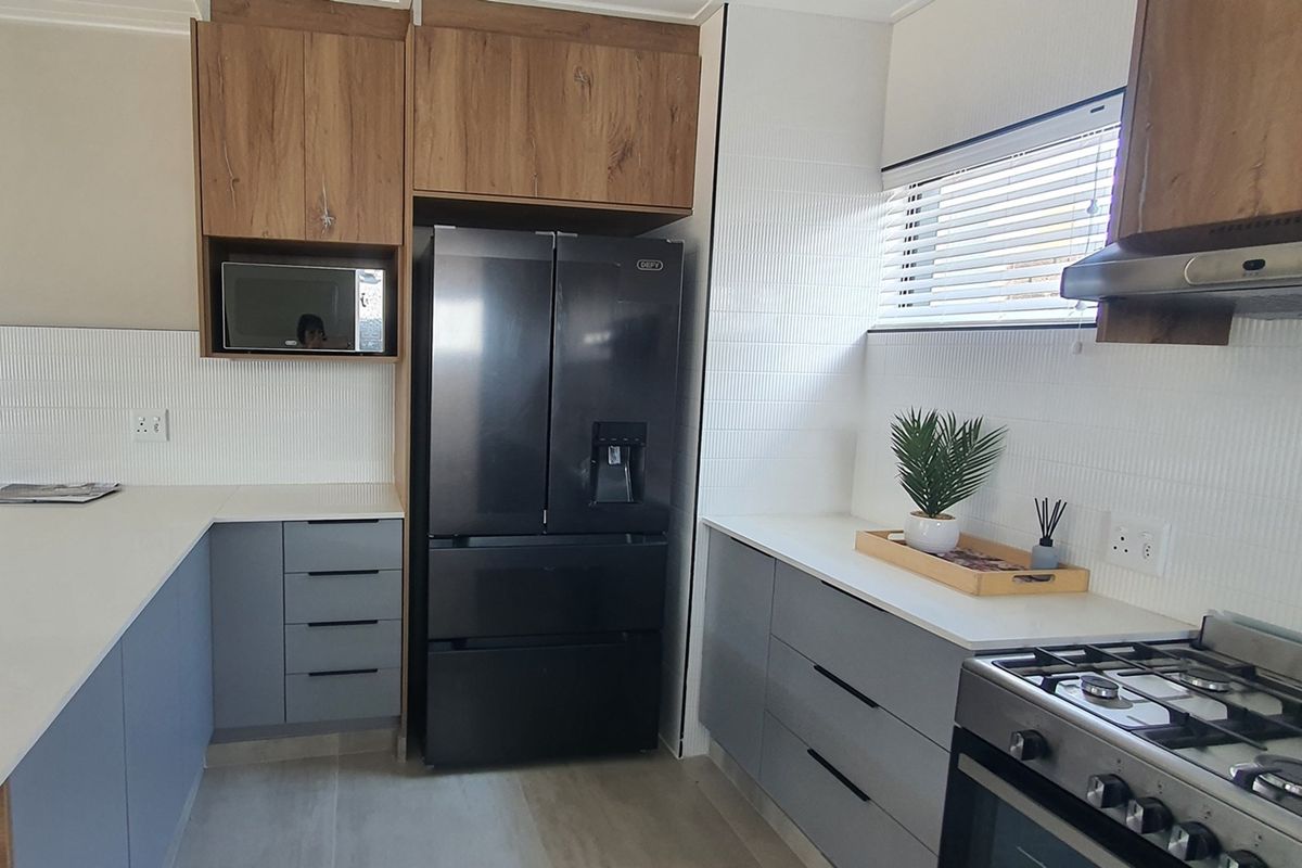 Modern kitchen featuring two-tone cabinetry, white tiled backsplash, stone countertops, and a built-in microwave space.