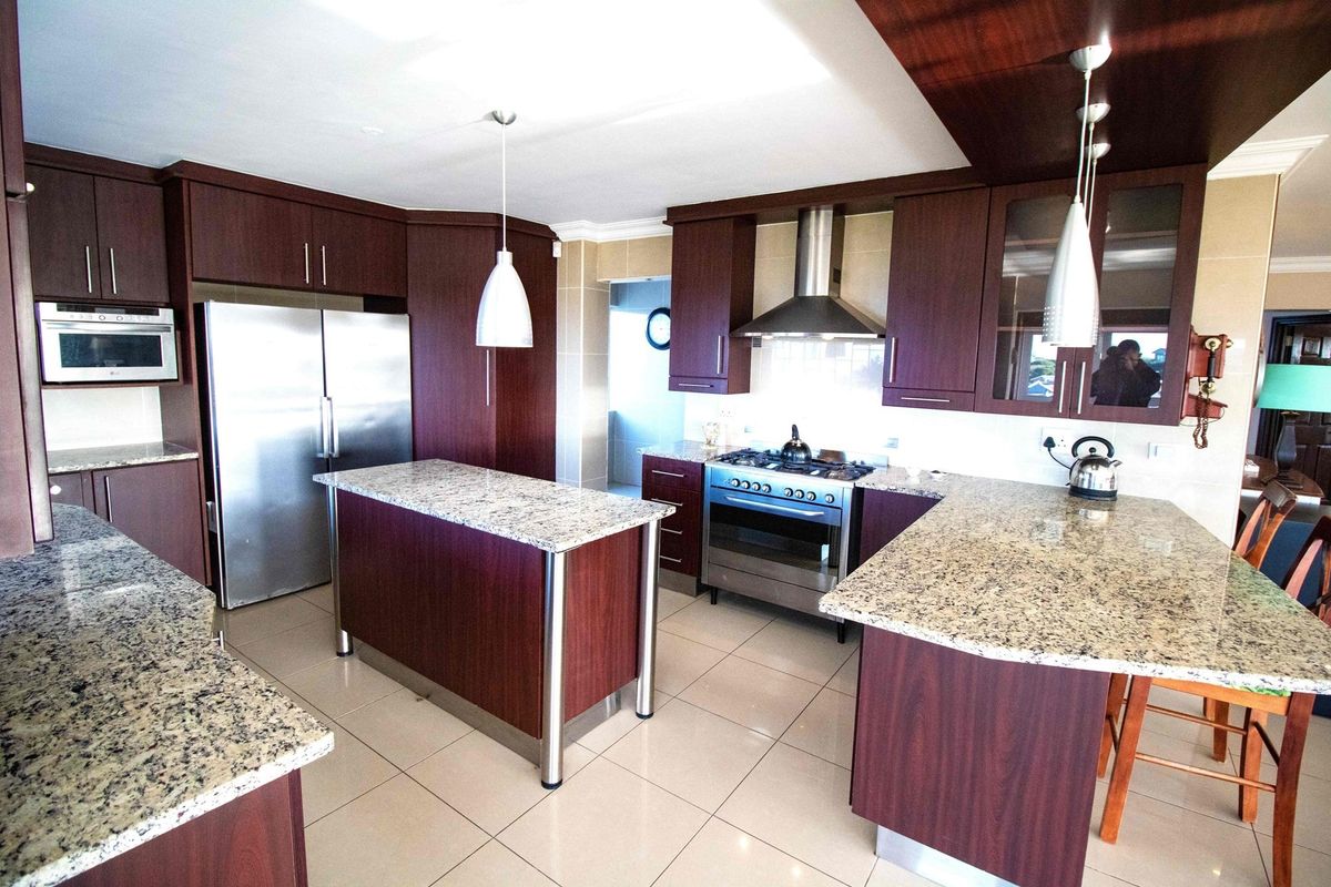 Modern kitchen featuring dark wood cabinetry, granite countertops, a central island, stainless steel gas stove, extractor fan, and built-in microwave.
