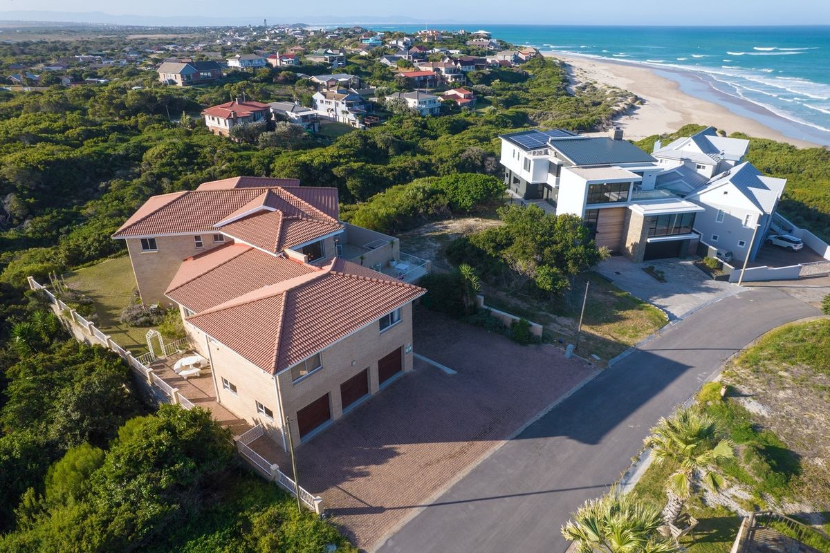 Aerial view of a coastal residential property featuring a multi-level house with a tiled roof, paved driveway, and triple garage.