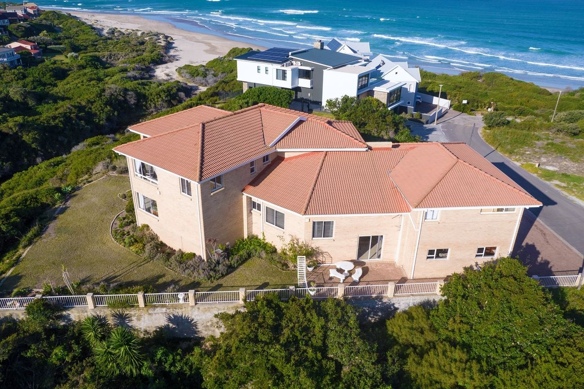 Aerial view of a large multi-level brick residence with a terracotta tiled roof, situated in a coastal location near the beach.