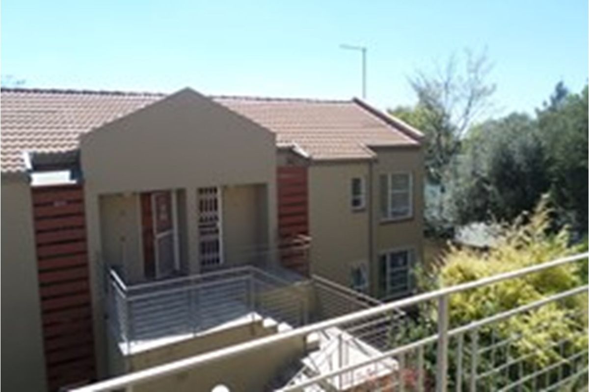 Exterior view of a townhouse complex featuring tiled roofing, balcony with metal railings, and neutral-toned facade finishes.