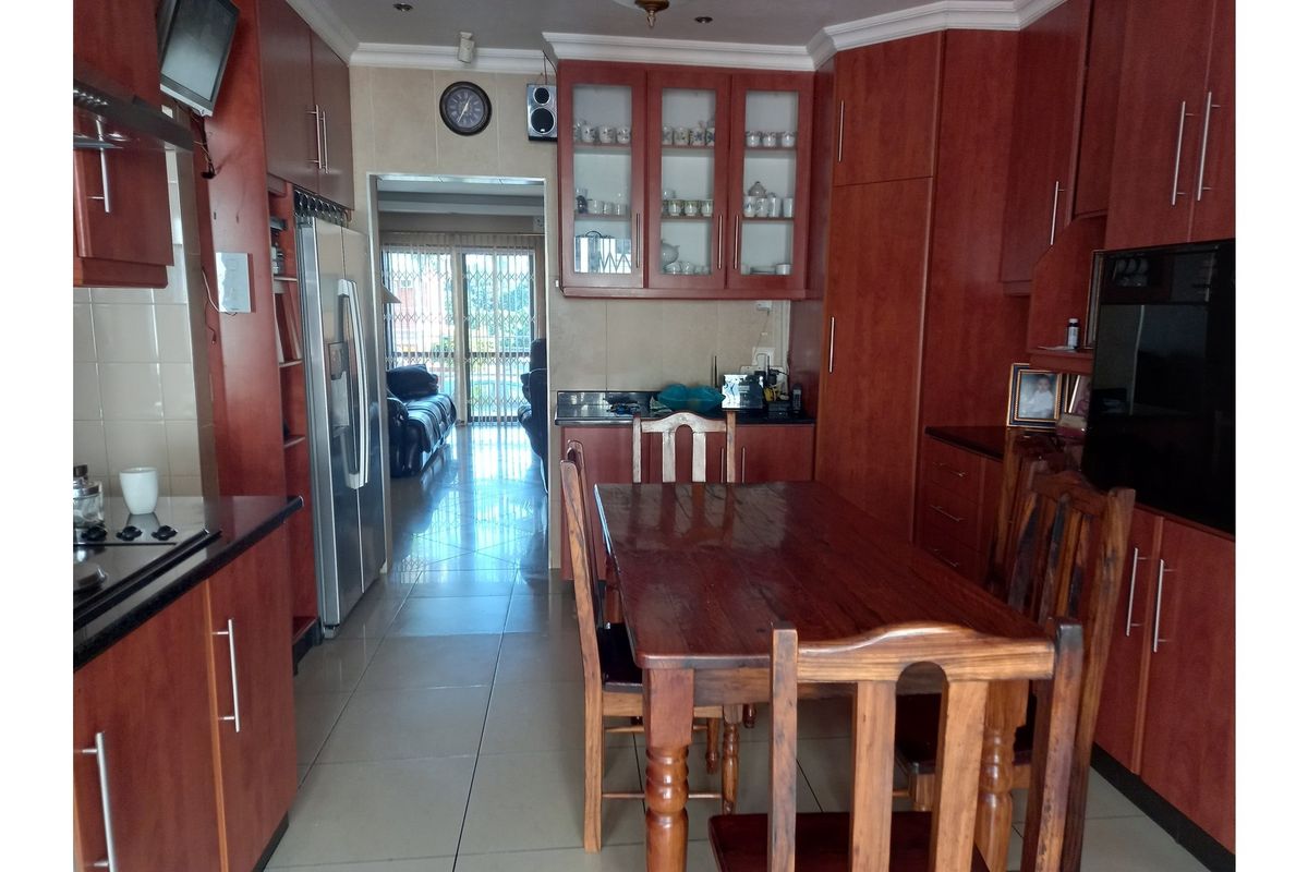 A functional kitchen featuring dark wood cabinetry, granite countertops, and a built-in hob, with an adjacent dining area and tiled flooring throughout.