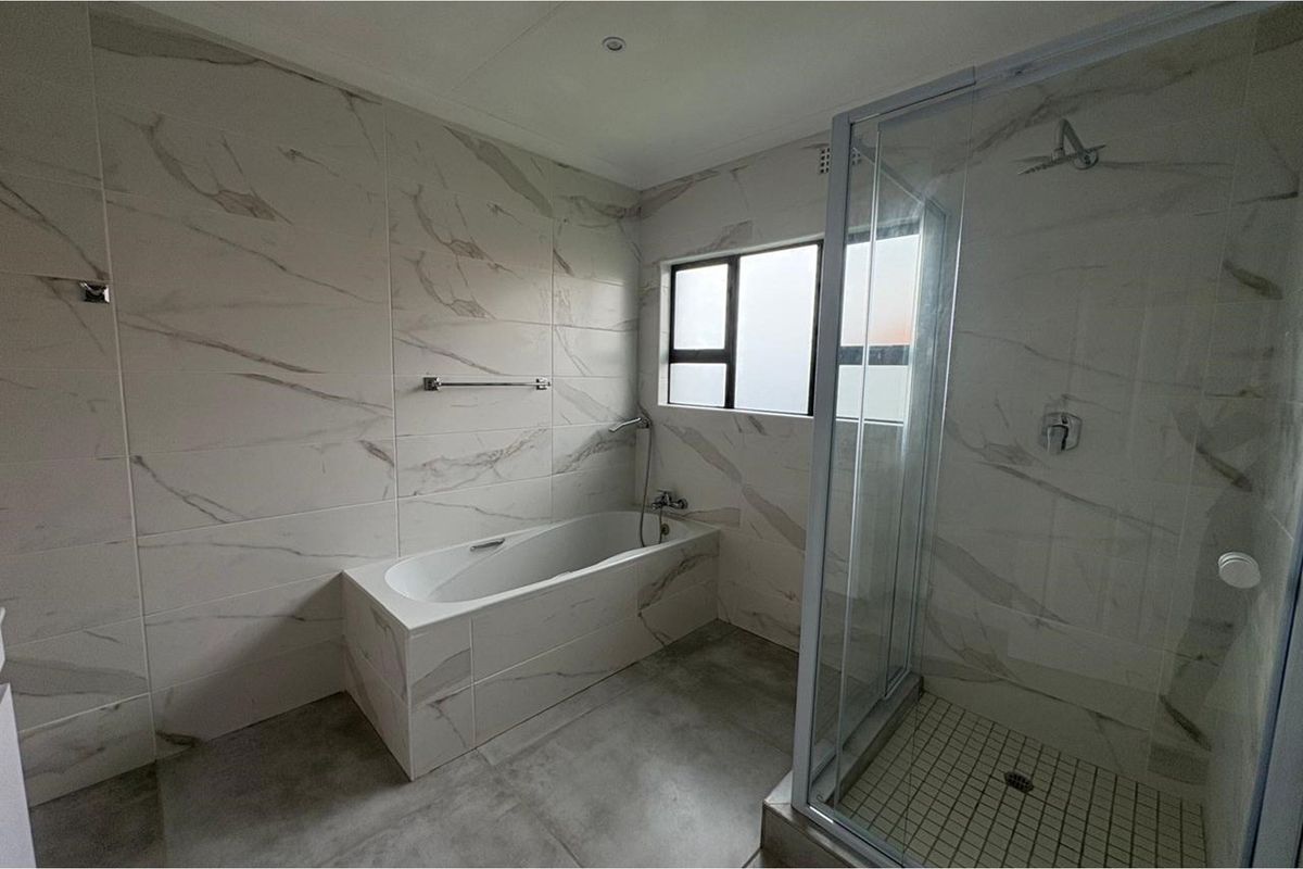 Modern bathroom featuring floor-to-ceiling marble-look wall tiles, a built-in bathtub, and a separate glass-enclosed shower with a tiled base.