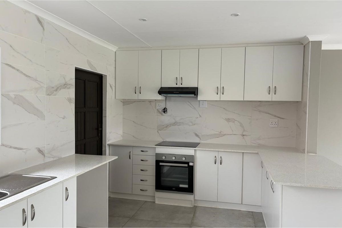 Modern kitchen featuring white cabinetry, marble-look tiled splashbacks, stone-style countertops, a built-in oven, and an extractor fan.