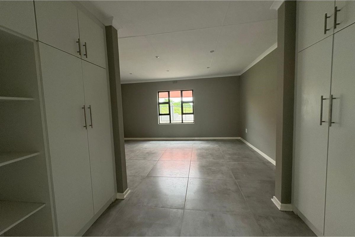 A spacious, empty living area featuring large format floor tiles, neutral grey walls, and extensive built-in cabinetry for ample storage.