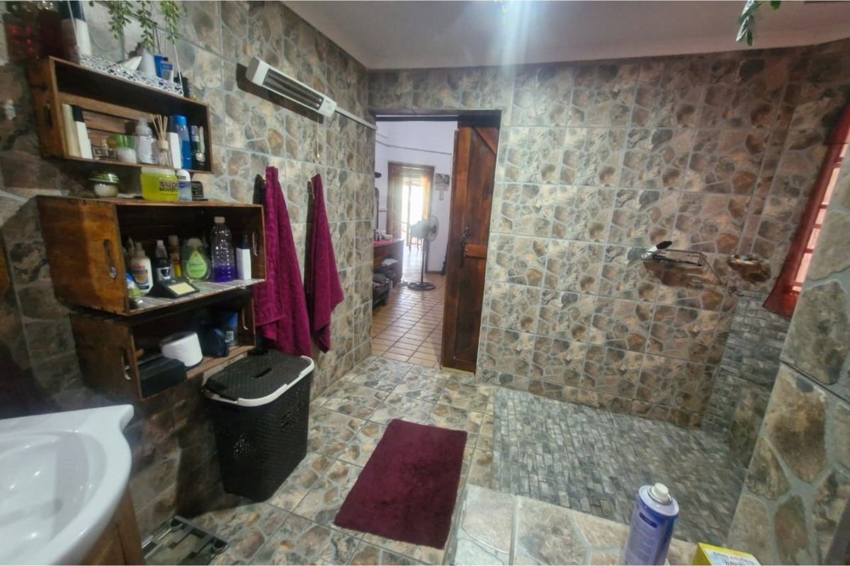 A bathroom featuring full-height stone-effect wall tiling, a walk-in shower area, and a wooden door leading to the adjacent living space.