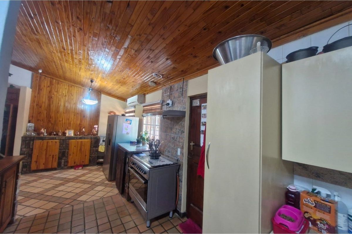 A rustic kitchen featuring wood-paneled ceilings, tiled flooring, and built-in cabinetry with a freestanding stove and extractor fan.